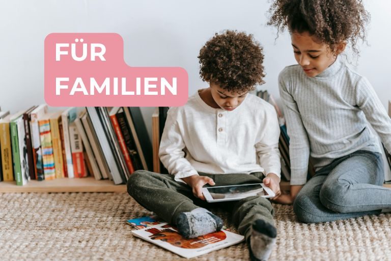 Junge und Mädchen sitzen vor einer Reihe Bücher und schauen gemeinsam auf ein Tablet, Schriftzug: Für Familien